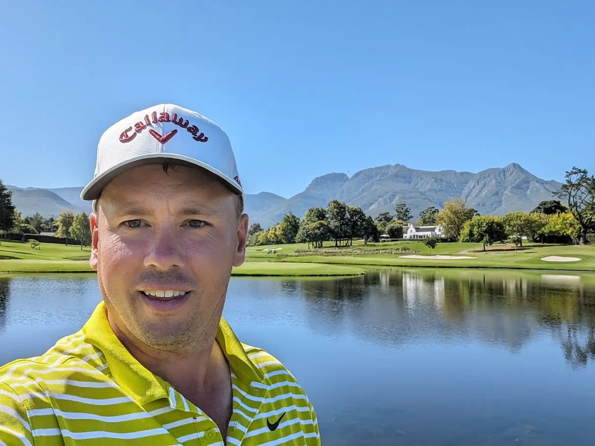 Sean Alexander on a golf course beside a lake, with mountains in the background